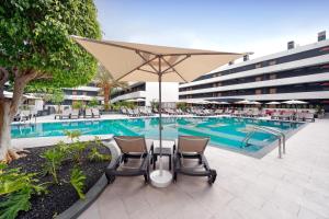 a pool with chairs and an umbrella next to a building at HOVIMA Suites Costa Adeje in Adeje