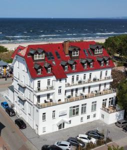 un grand bâtiment blanc avec un toit rouge à côté de l'océan dans l'établissement Strandhotel Ostende, à Ahlbeck