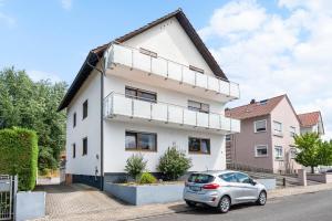 a white house with a car parked in front of it at Ruhiges und zentrales Apartment in Hüttenfeld in Lampertheim