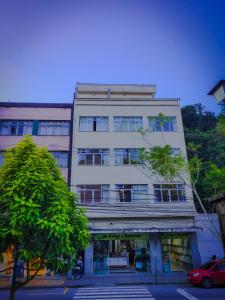 um edifício branco alto com uma árvore em frente em Dom Pedro Hotel em Petrópolis