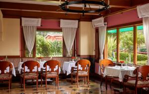 un comedor con mesas, sillas y ventanas en Fortune Resort Sullivan Court, Ooty - Member ITC's Hotel Group, en Ooty