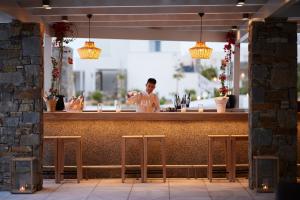 Un uomo in piedi dietro un bancone con degli sgabelli di Summer Senses Luxury Resort a Logaras