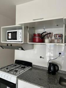 a white kitchen with a stove and a microwave at MC Departamentos Villa Allende in Villa Allende