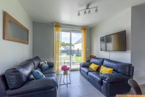 Sala de estar con 2 sofás de cuero y TV en Les Fuchsias - Maison proche de la mer, en Asnelles