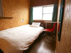 館山市にある館山ウィールズゲストハウスの小さなベッドルーム(ベッド1台、赤い椅子付)
