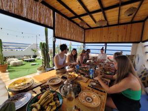 a group of people sitting around a table with food at Good Wave Surf House in Tamraght Ou Fella