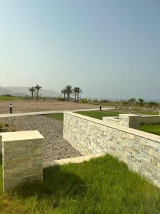 a stone wall with palm trees in the background at Jebel Sifah Golf View Apartment in Muscat