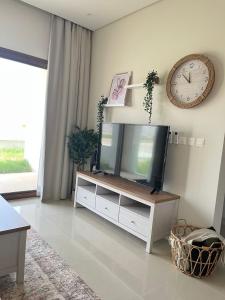 uma sala de estar com televisão e um relógio na parede em Jebel Sifah Golf View Apartment em Mascate