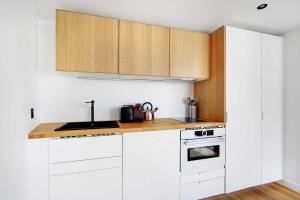 a white kitchen with wooden cabinets and a sink at Cosy renovated 1BDR on rue des Archives Marais Clim 5 in Paris