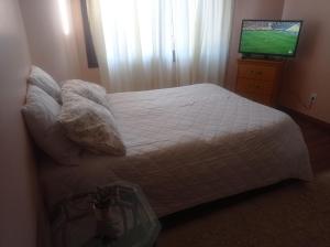 um quarto com uma cama branca e uma televisão em Residencial Pine House em Canela