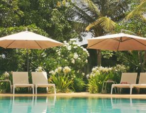- deux parasols et des chaises à côté de la piscine dans l'établissement La Maison Vanille, à Ngaparou