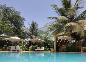 a swimming pool with umbrellas and chairs and palm trees at La Maison Vanille in Ngaparou