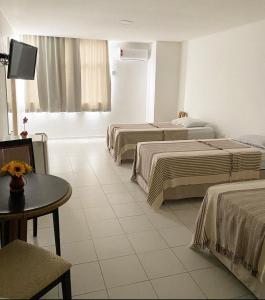 a hotel room with three beds and a table at Majestic Hotel in Campina Grande