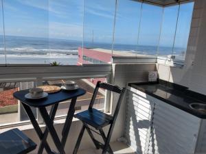 a table and chair on a balcony with a view of the ocean at Aconchegante Apto Praia do Centro in Itanhaém