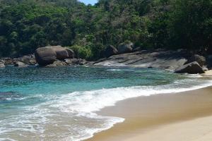a beach with rocks and blue water and a mountain at Chalés da Barra Ilhabela in Ilhabela