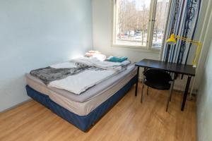 a small bed in a room with a desk and a window at Cozy budget room w/ balcony in shared apartment in Vantaa