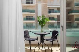 een tafel met stoelen en een vaas met bloemen op een balkon bij Luxury living 100 meter from the beach - by Edom in Eilat