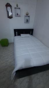 Cama blanca en habitación con reloj en la pared en Apartamento Cómodo en Medellín, en Bello