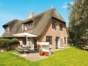 a house with a thatched roof with a table and an umbrella at Salig-Hues in Kampen