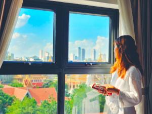 a woman standing in front of a window holding a remote control at Le Botum Hotel in Phnom Penh