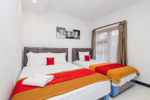 two beds in a white room with red and orange sheets at RedDoorz Syariah At Wisma Djokorio Poncokusumo in Gubukklakah