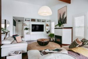 uma sala de estar com mobiliário branco e uma televisão em Jungle Cubby - by Coast Hosting em Terrigal