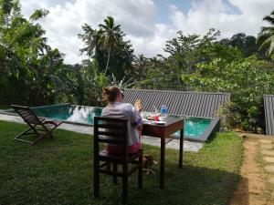 une femme assise à une table à côté d'une piscine dans l'établissement Rainforest Chalets - Rainforest Tours,Pool And Ac, à Deniyaya