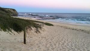 a beach with a fence in the sand and the ocean at Lighthouse Palms in Ulladulla