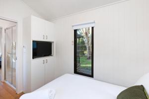 a white bedroom with a bed and a tv at Reflections Moonee Beach - Holiday Park in Moonee Beach