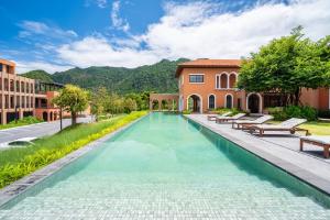 a large swimming pool with benches and a house at Locanda Villanova Bed & Breakfast in Pak Chong