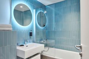 a blue tiled bathroom with a sink and mirror at Hotel Magenta 38 by Happyculture in Paris