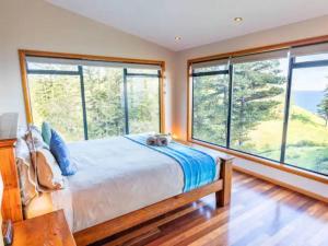 a bedroom with a large bed and large windows at King Tide House - Ocean Views in Burnt Pine