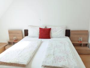 uma cama com lençóis brancos e uma almofada vermelha em Apartments Wallas em Bovec