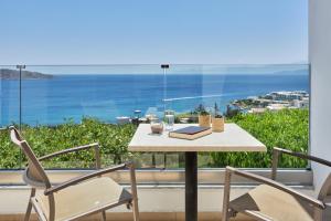 een tafel en stoelen op een balkon met uitzicht op de oceaan bij Elounda Ilion Hotel Bungalows in Elounda