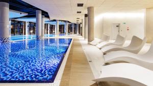 a swimming pool with white chairs in a building at Seaside Luxury Apartament in Kołobrzeg