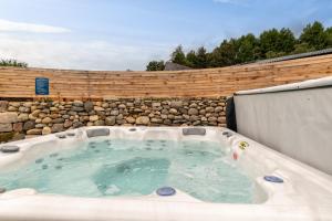 una bañera de hidromasaje en un patio trasero con una pared de piedra en Enchanting Tiny House with wood burner and hot tub in Cairngorms en Ballater