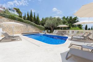 a swimming pool with chairs and umbrellas at Villa Maitreya By MENORCARENTALS in Son Bou