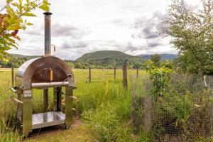 an outdoor oven sitting in a field next to a fence at Aileen - Unique tiny house with wood fired roll top bath in heart of the Cairngorms in Ballater