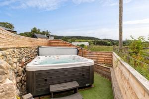 un bain à remous dans un jardin avec un mur en pierre dans l'établissement Charming boutique forest view cabin with hot tub in Ballater, à Ballater