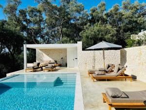 a pool with chairs and an umbrella next to a house at Luxury Stone Houses Corfu in Píthos