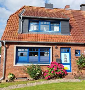 ein rotes Backsteinhaus mit blauen Fenstern und Blumen in der Unterkunft Voslapper Seeluft in Wilhelmshaven