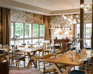 een restaurant met houten tafels, stoelen en ramen bij Demeures de Campagne Parc du Coudray - Barbizon in Le Coudray-Montceaux