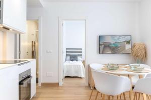 a white kitchen with a table and white chairs at APARTAMENTOS CARMEN in Maro