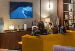 2 femmes assises sur un canapé en regardant une télévision dans l'établissement Hôtel Burdigala by Inwood Hotels, à Bordeaux