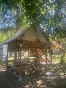 a tree house with a thatched roof under a tree at Le bivouac-tente chez Camille in Veynes