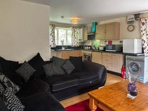 a living room with a black couch and a kitchen at Woodside Fishery - The Plover in Cleobury Mortimer