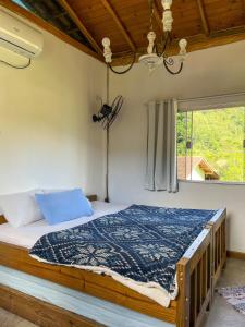a bedroom with a bed with a blue comforter and a window at Flat aconchegante próximo à Trindade e Paraty in Paraty
