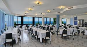 a restaurant with white tables and chairs and windows at Hotel Venus in Gabicce Mare