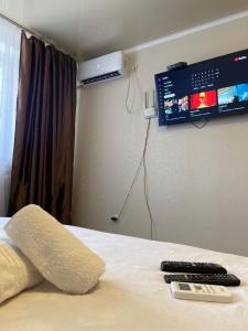 a bed with two remote controls and a tv on the wall at микрорайон Астана с кодовым замком in Uralsk