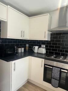 a kitchen with white cabinets and a black tile wall at CAPRI 13 SA- Nice ’n’ New, close to Uni and M1/J23 in Loughborough
